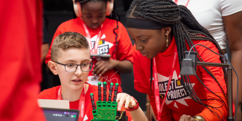 Two young tech creators adjust a robotic hand at Coolest Projects UK 2024.