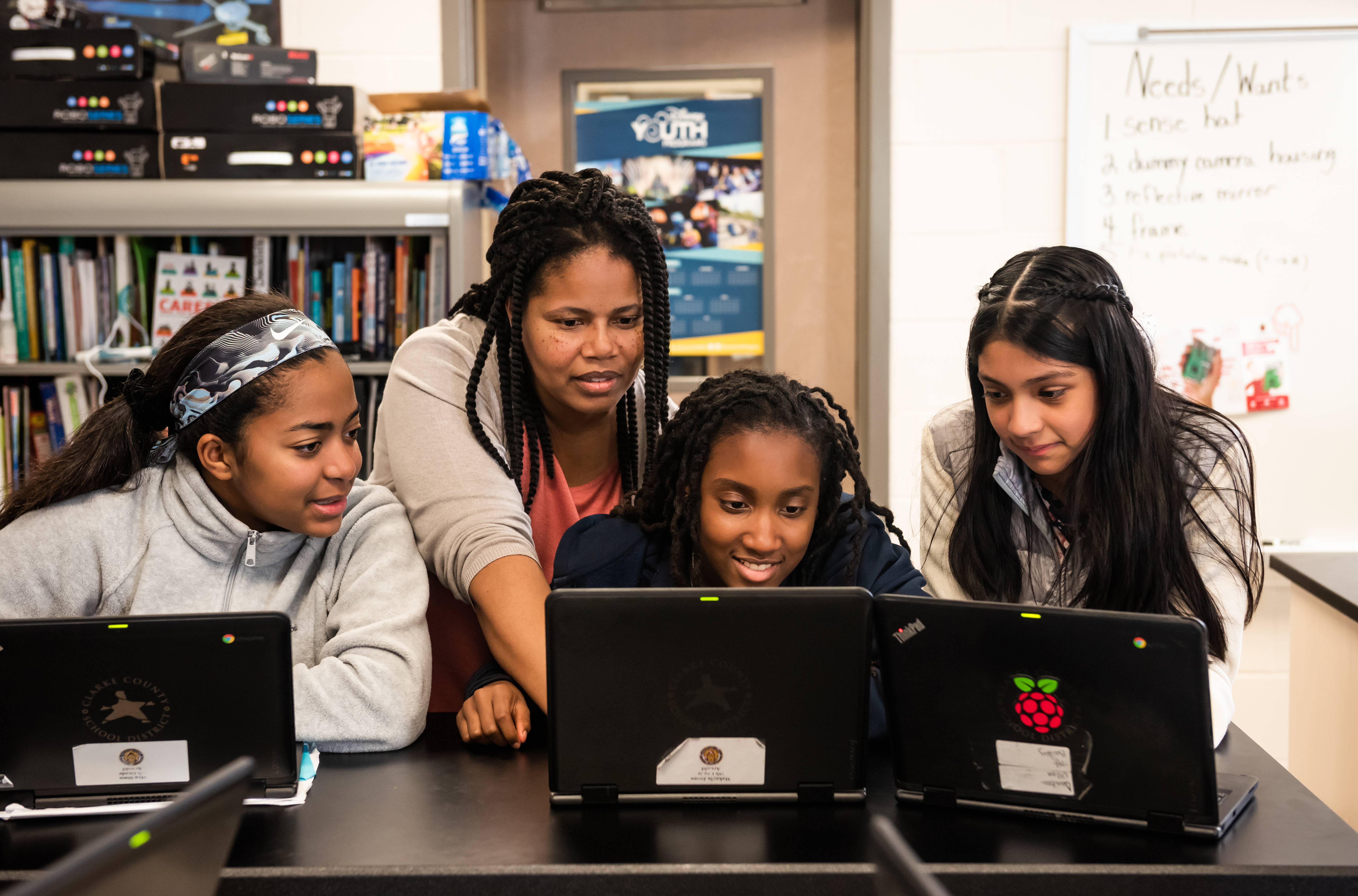 A computing educator with three students at laptops in a classroom.