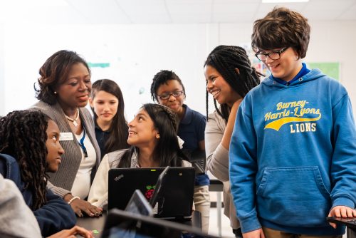 A group of young people and educators smiling while engaging with a computer.