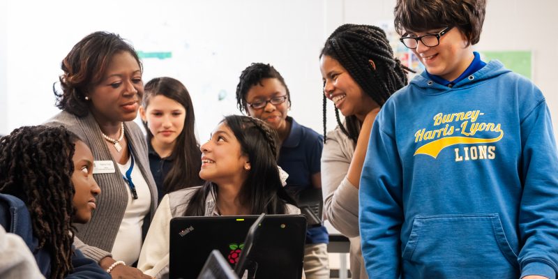 A group of young people and educators smiling while engaging with a computer