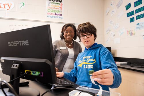 A teacher assisting a young person with a coding project.