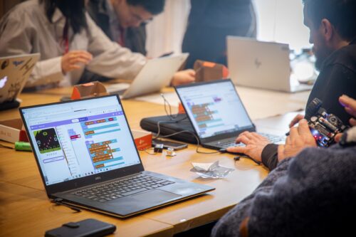 Photo of educators collaborating on various projects at a desk, with laptops open displaying the Scratch Editor.