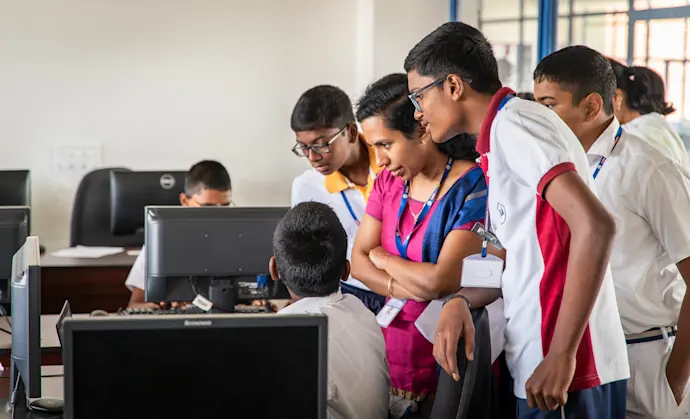 A mentor surrounded by young people in a coding club session.