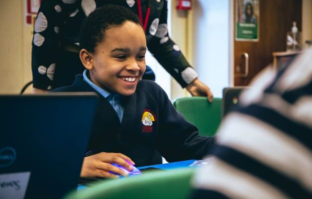 A young person smiles while using a laptop.