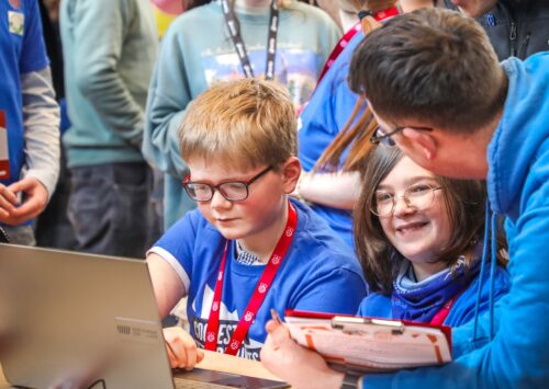 Two young people share a project on their laptop with a judge at Coolest Projects.