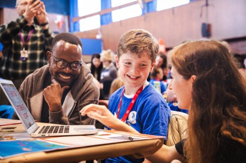 Photo of a young creator showcasing they're project to two Raspberry Pi Foundation judges.