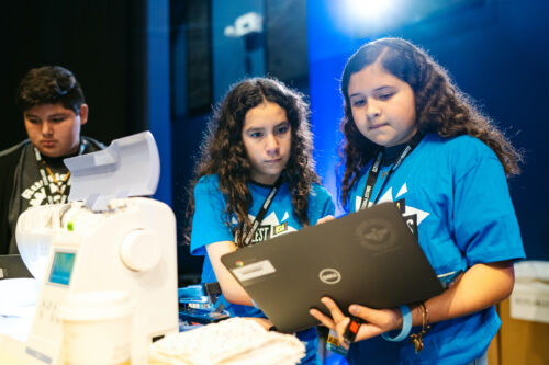 Two young coders work on their tech project on a laptop to control a sewing machine for Coolest Projects.