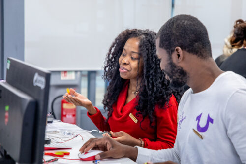 Two educators discuss something at a desktop computer.