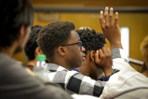 An undergraduate student is raising his hand up during a lecture at a university.