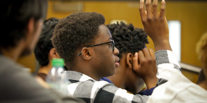 An undergraduate student is raising his hand up during a lecture at a university.