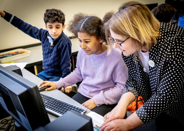 An educator is helping two young learners with a coding task.