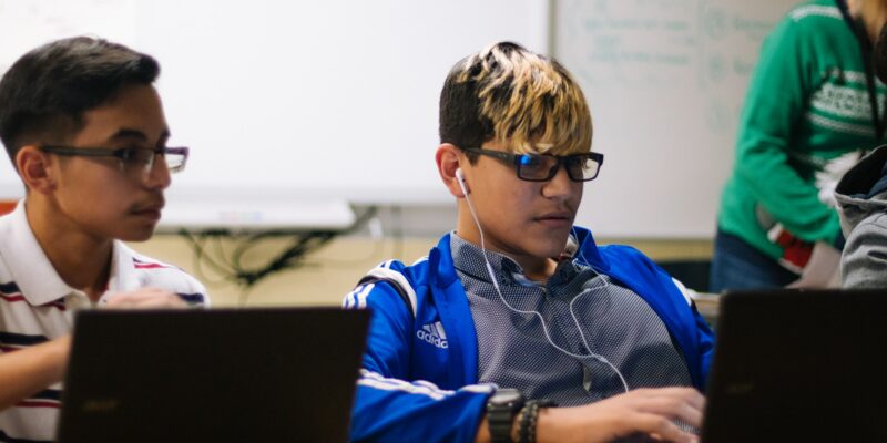 Two boys at laptops in a classroom.