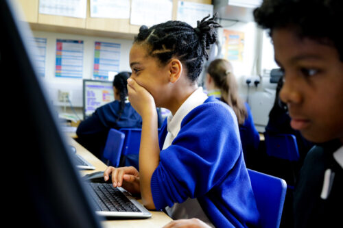 In a computing classroom, a girl laughs at what she sees on the screen.