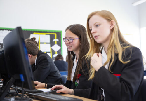 Two learners at computers in a classroom.