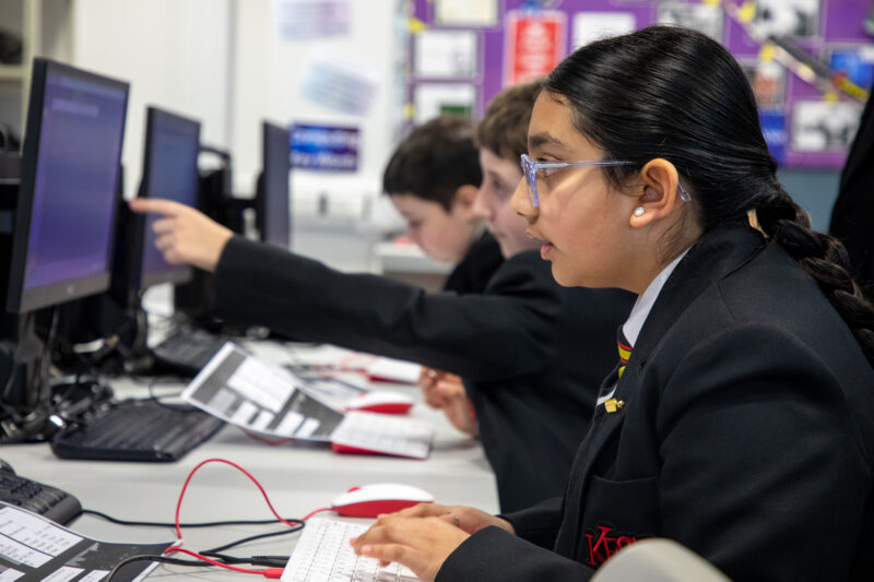 Computer science students at a desktop computer in a classroom.