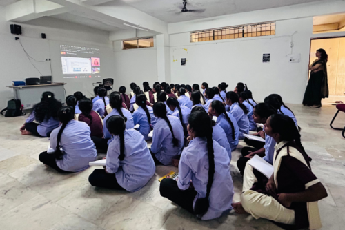 Students sit in a classroom and watch the lecture slides. 