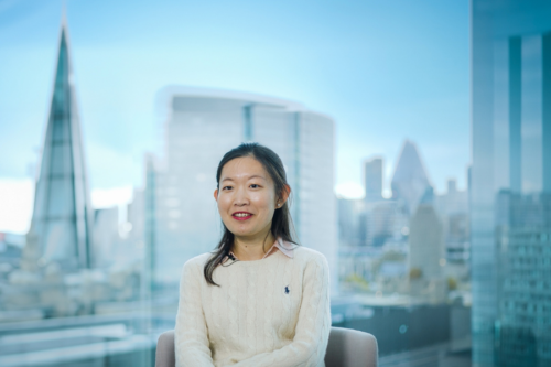 A woman is pictured sitting in the office. There's a window behind her with a view of the London skyline. 